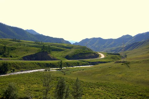 A picturesque valley with a river flowing through it, surrounded by fields and coniferous forests. Altai, Siberia, Russia.