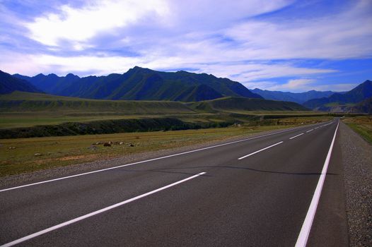 Road landscape, paved straight road goes beyond the horizon through the mountains. Kurai steppe, Altai, Russia.