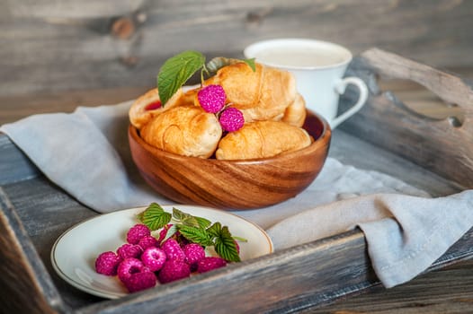 Croissants with raspberries on a wooden tray. The concept of a wholesome breakfast