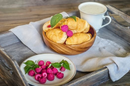 Croissants with raspberries on a wooden tray. The concept of a wholesome breakfast