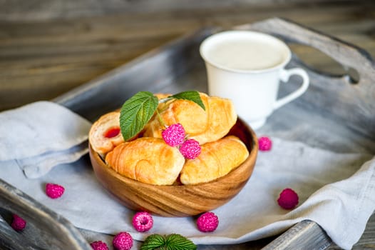 Croissants with raspberries on a wooden tray. The concept of a wholesome breakfast