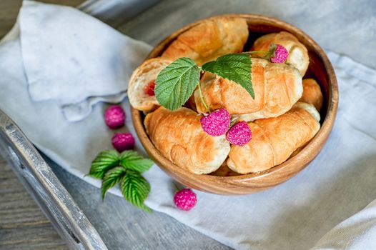 Croissants with raspberries on a wooden tray. The concept of a wholesome breakfast