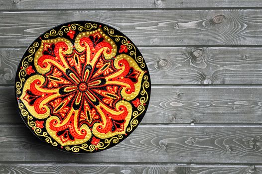 Decorative ceramic plate, hand painted with acrylic paints on a wooden background. Closeup with place for text