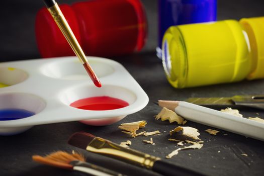 Closeup artist paint brush above color plate and poster color bottle on table. Concept of art education.