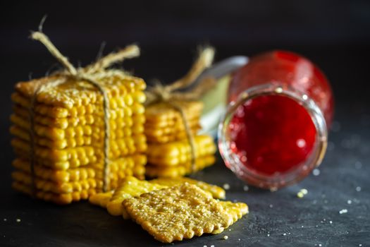 Crackers are tied with hemp rope and strawberry jam bottle on table in dark background.