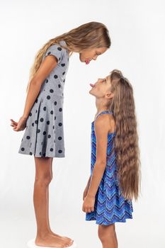 A girl stands on a chair, another girl stands nearby, show each other tongues