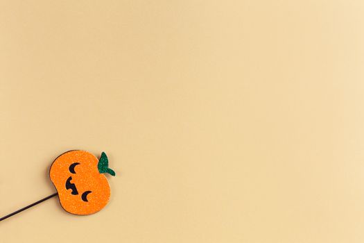 Halloween party accessory, shiny pumpkin with cute creepy faces. Pastel yellow background, place for text. Holiday flat lay. Minimal style. Horizontal.