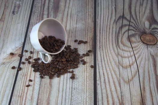 The coffee beans are scattered inside and around the overturned white coffee cup.