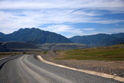 A dirt road with a fence running through the mountains and the valley. Gorny Altai, Siberia, Russia.