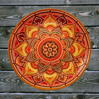 Decorative ceramic plate, hand painted dot pattern with acrylic paints on a gray wooden background. A square photo. Closeup