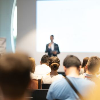 Male speaker giving a talk in conference hall at business event. Audience at the conference hall. Business and Entrepreneurship concept. Focus on unrecognizable people in audience.