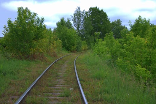 An old and abandoned railway line turns through a summer forest.