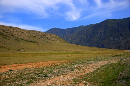 Gravel road surrounded by high gentle mountains. Altai, Siberia, Russia