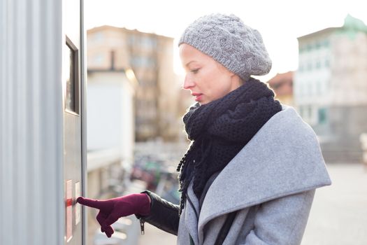 Casual woman buying public transport tickets on city urban vedning machine on cold winter day in Ljubljana, Slovenia.