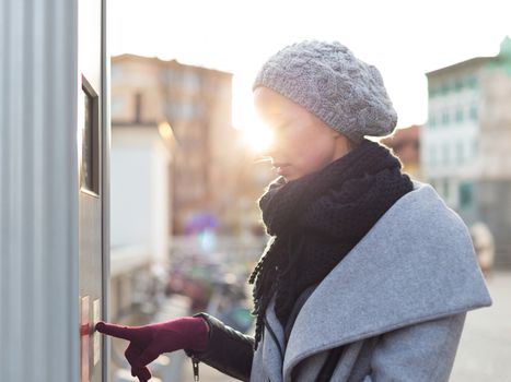 Casual woman buying public transport tickets on city urban vedning machine on cold winter day in Ljubljana, Slovenia.