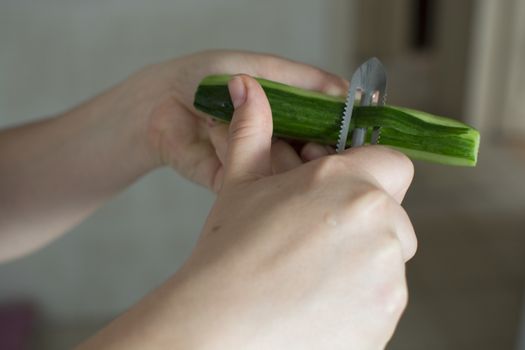 A woman's hands. Cleans the cucumber shell. Preparing for meals