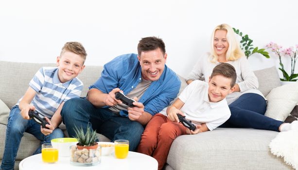 Happy young family playing videogame console on TV. Spending quality leisure time with children and family concept. Gaming consoles are generic and debranded.