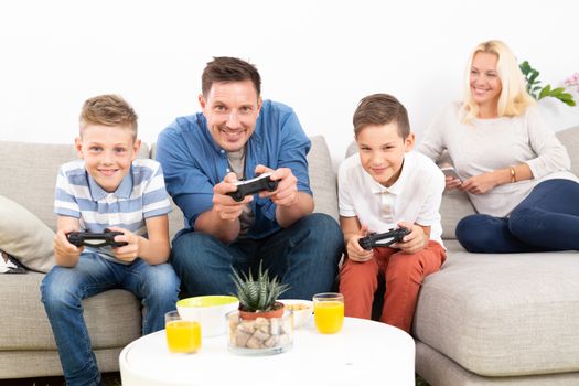 Happy young family playing videogame console on TV. Spending quality leisure time with children and family concept. Gaming consoles are generic and debranded.