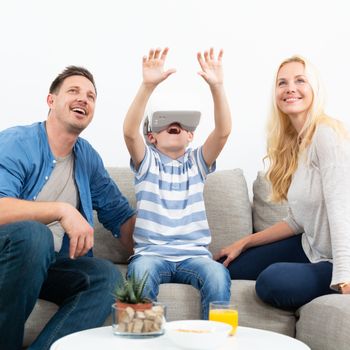 Happy caucasian family at home on living room sofa having fun playing games using virtual reality headset.