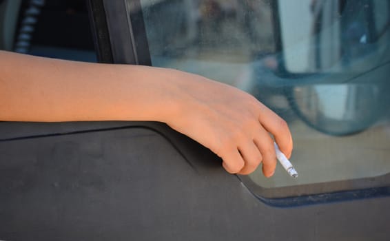 the woman is smoking. hand and cigarette removed from the car window