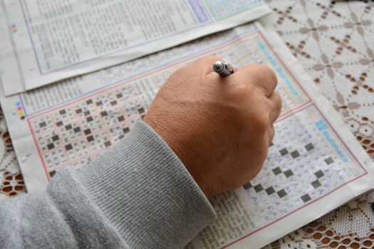 old man hands. He holds a pencil in his hand. solving puzzles.