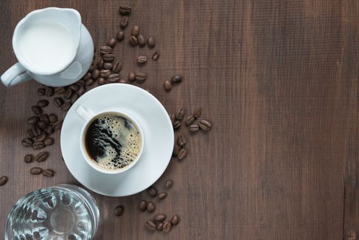 Cup of coffee, cream in a milk jug, glass of water and coffe beans on the wooden table with copy-space, top view