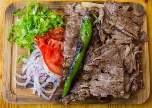 "Döner Kebab" is served with fresh greens on the board. 
famous turkish food. Döner kebab is a Turkish kebab, made of meat cooked on a vertical rotisserie.