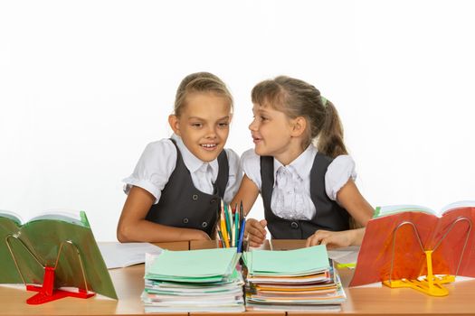 Two girls whisper while sitting at a desk