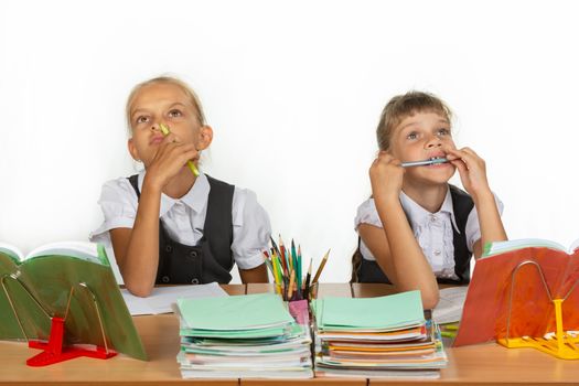 Two schoolgirls pensively and funny sit at the table and look up