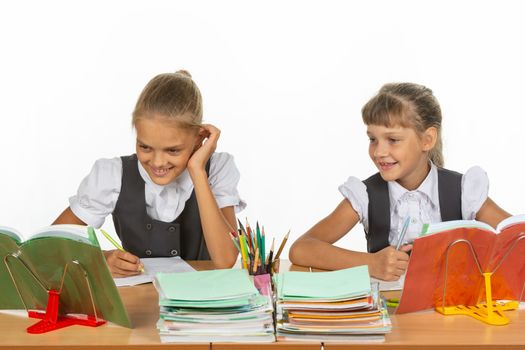 Two schoolgirls are sitting at a desk and cheerfully looking at the textbook