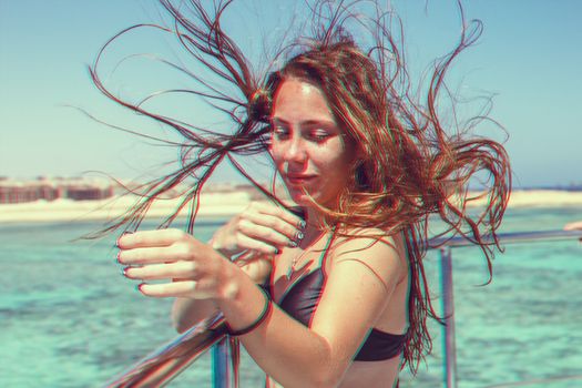 Young brunette girl in a black bathing suit develop hair on a yacht at sea. Exotic beauty. A high resolution. Glitch vintage shabby coral turquoise effect.