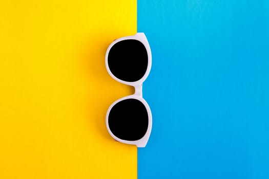 Sunny stylish white sunglasses on a bright blue-cyan and yellow-orange background, top view, isolated. Copy space. Flat lay.