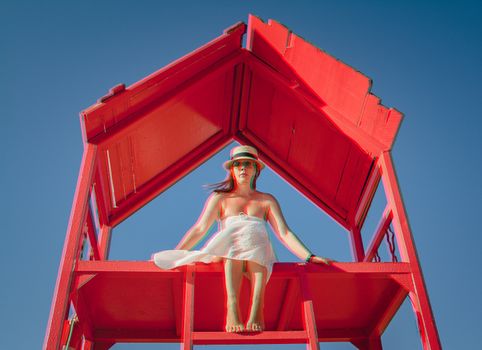 A young blonde girl in a straw hat and white dress sits on a red rescue tower on the beach of Egypt against a blue sky. Glitch Vintage Shabby Coral Turquoise Anaglyph 3D Effect.