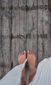 Beautiful female bare bare tanned legs with pink pedicure on wooden beach flooring. Top view, copy space.