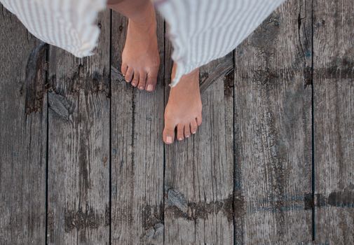 Beautiful female bare bare tanned legs with pink pedicure on wooden beach flooring. Top view, copy space.