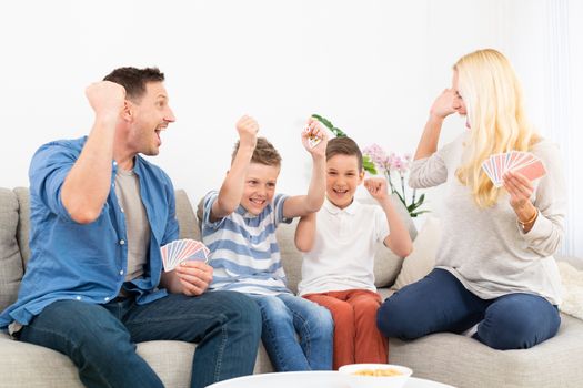Happy family playing card game on living room sofa at home and having fun together celebrating the game winner.