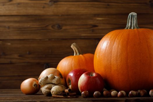 Autumn harvest still life with pumpkins, apples, hazelnut, ginger, onion and cinnamon on wooden background