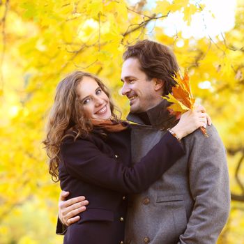 love, relationship, family and people concept - couple with maple leaves hug in autumn park