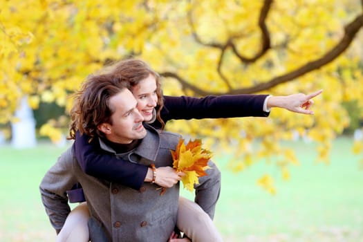 Couple in autumn park having fun, smiling man carrying woman piggyback outdoor