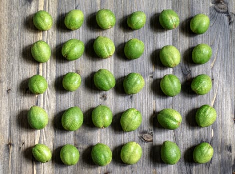 Young green fruits of walnuts lie in rows on a gray wooden background