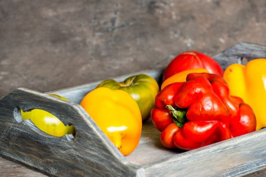 Imperfect natural peppers and tomatoes on an old wooden tray on a dark background. Healthy eating concept. Copy Space.