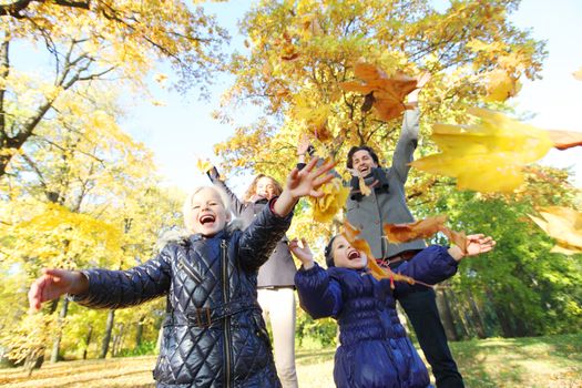 Happy smiling family of parents and children playing throwing leaves in autumn park