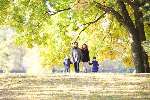 Happy smiling family of parents and children walking together holding hands in autumn park