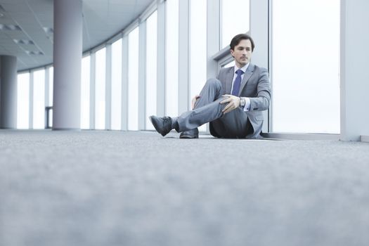 Businessman sitting on floor in office near window