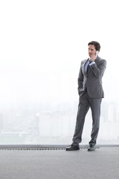 Businessman standing near window, looking at city and talking by phone