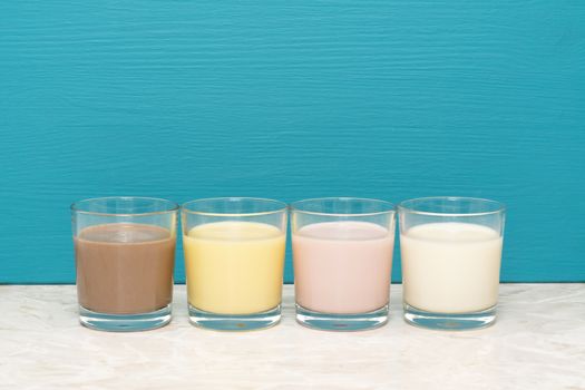 Chocolate, banana and strawberry milkshakes and fresh milk in glass tumblers against a teal background