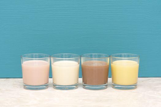 Flavoured milkshakes - strawberry, chocolate and banana - and fresh creamy milk in glass tumblers against a teal background