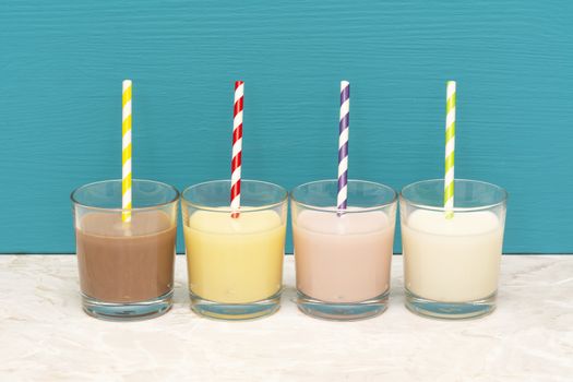 Chocolate, banana and strawberry milkshakes and fresh milk with retro paper straws in glass tumblers with a teal background