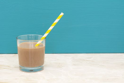 Thick chocolate milkshake with a retro paper straw in a glass tumbler with a teal background and copy space