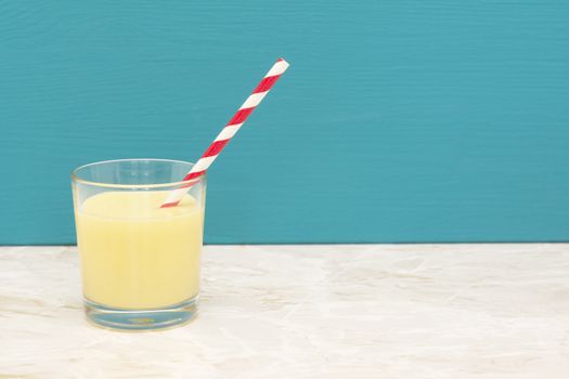 Tasty banana milkshake with a retro paper straw in a glass tumbler with a teal background and copy space